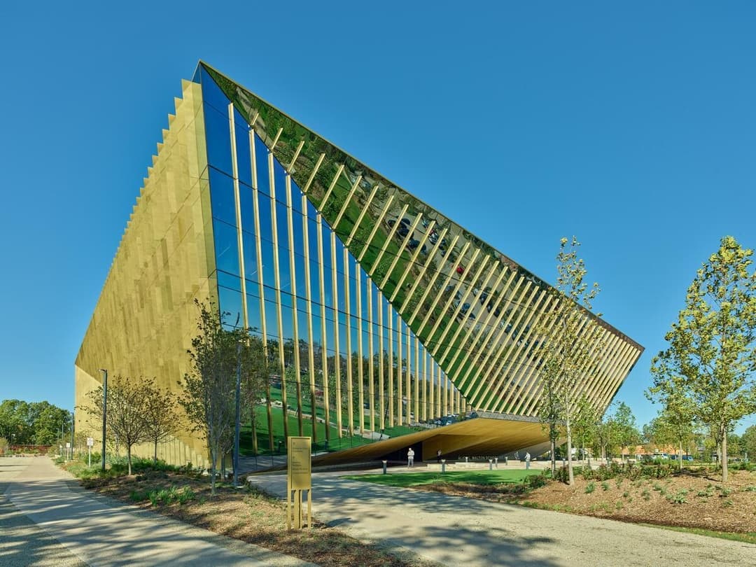 Exterior shot of a tall building with angular points and all surfaces covered in windows lined with brass fins